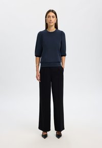 Maglione navy con maniche a sbuffo corte e orlo a coste, abbinato a pantaloni neri a vita alta a gamba wide e tacchi a punta neri.