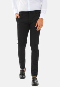Pantaloni neri slim fit realizzati in tessuto testurizzato, dotati di chiusura con bottone e tasche laterali, abbinati a mocassini neri.