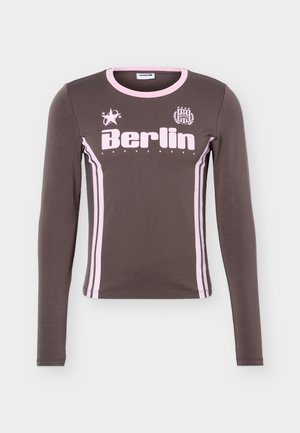 Chemise grise à manches longues avec bordure rose, rayures verticales sur les côtés et texte "Berlin" avec logos étoile et blason sur la poitrine.