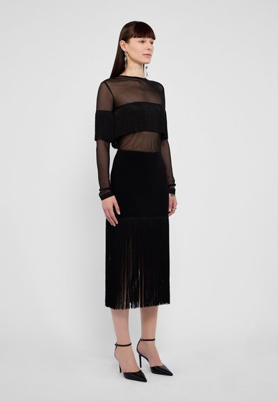 Sort kjole med en gennemsigtig, frynsedetalje i toppen og en tætsiddende nederdel med frynser i kanten. Glat tekstur, med en elegant silhuet og ankelremssko.
