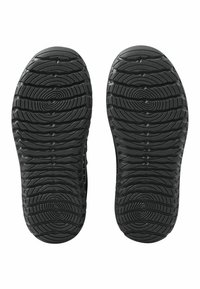 Suole nere delle scarpe con un motivo testurizzato a forma di onda e grip circolari per la trazione. Il materiale appare gommoso e resistente, con una finitura opaca.