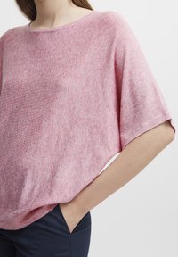 Roze melange gebreid top met een ontspannen pasvorm, wijde korte mouwen en een ronde hals. Draagt over een donkere broek, wat de zachte textuur benadrukt.