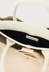 Sac à main beige texturé avec deux poignées, ferrures dorées et doublure intérieure noire. Comprend une petite étiquette intérieure.