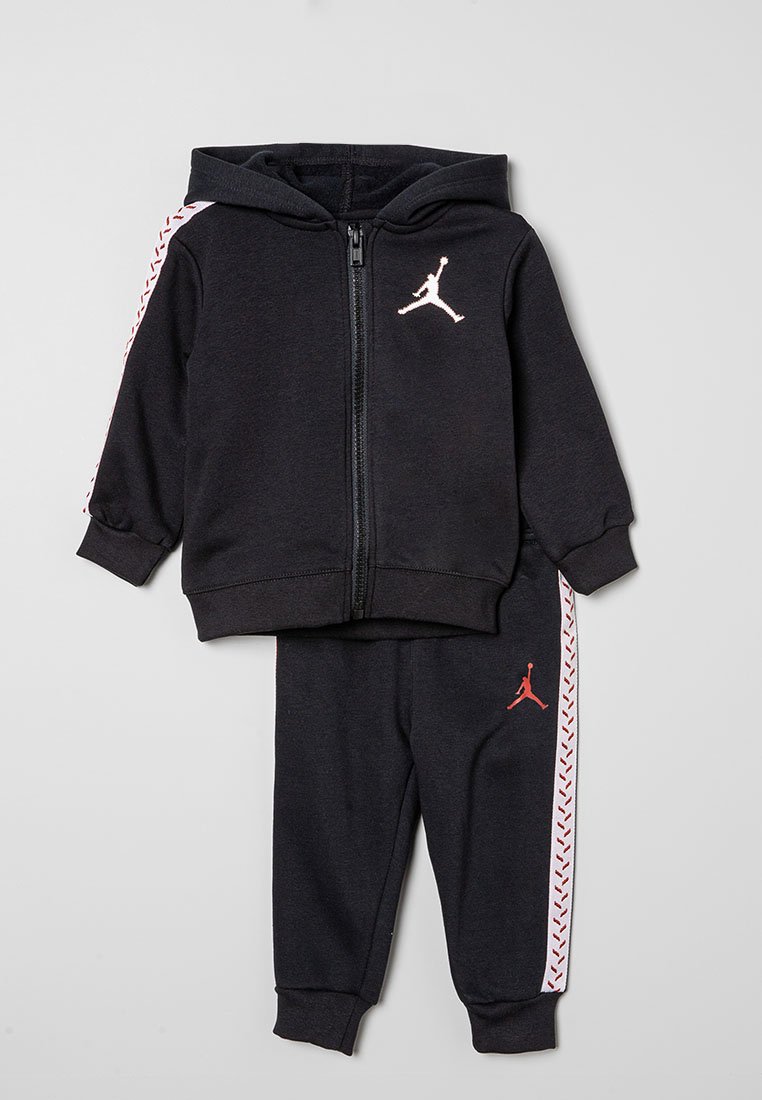 Completo felpa e pantaloni per bambino nero con strisce a motivo bianco e rosso sulle maniche e sulle gambe, dotato di un logo sportivo sul petto e sulla coscia.
