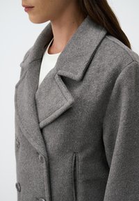 Cappotto grigio in misto lana con rever a notched, bottoni doppi, tasche laterali e una finitura testurizzata.