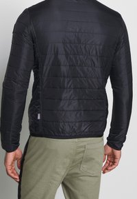 Schwarze Daunenjacke mit gestepptem Muster, die eine glatte Textur und eine taillierte Passform aufweist. Beinhaltet ein kleines Logo-Etikett in der Nähe des Saums.