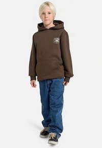 Ruskea huppari etutaskulla, jossa pieni logo. Yhdistetty löysiin sinisiin farkkuihin ja mustiin lenkkareihin. Suora siluetti.