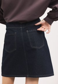 Gonna in denim scuro con vita aderente e silhouette a trapezio. Presenta due tasche posteriori e cuciture a contrasto. Tessuto strutturato.