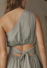 Bezrukávový, svetlosivý crop top s zhromaždeným pásom a detailom viazania na chrbte. Mäkka, textúrovaná látka s otvoreným dizajnom chrbta.
