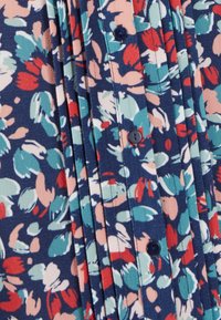 Blusa floreale di color blu navy, con un motivo di fiori rossi, rosa e verde menta. Realizzata in tessuto testurizzato, con dettagli di bottoni e pieghe.
