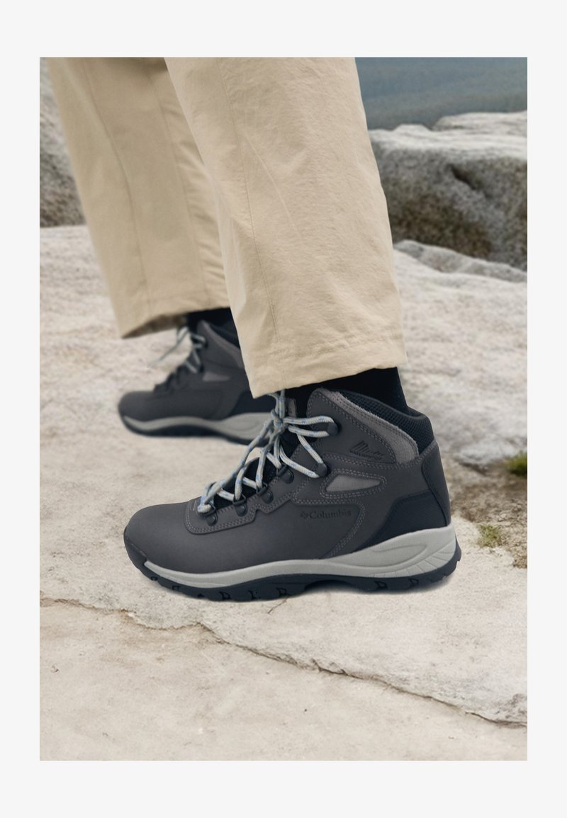 Scarpe da trekking Columbia in grigio scuro con accenti grigio chiaro, caratterizzate da un design alto, materiali in tessuto e sintetici, e suola robusta.