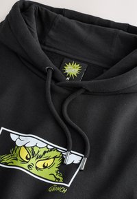 Zwarte hoodie van katoen met een grote Grinch-grafiek in groen en geel. Voorzien van een capuchon met trekkoord en een merkteken met gele accenten.