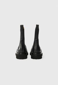 Bottines noires en cuir avec des panneaux élastiques sur les côtés, semelle en caoutchouc épaisse et finition lisse. Présente des coutures autour de la zone du talon.