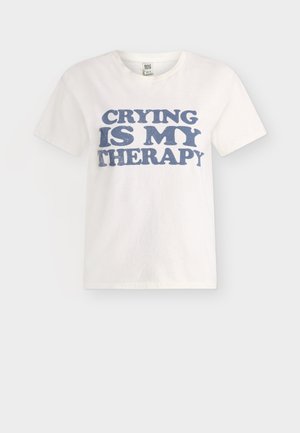 Vitt kortärmat T-shirt med blå text "CRYING IS MY THERAPY" på framsidan, visas mot en enkel ljus bakgrund.