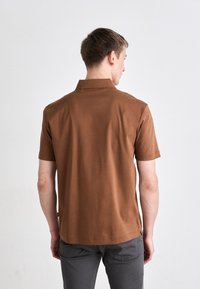 Rövidujjas barna pólóing, gallérral, sima textúrával és egyenes aljjal, egy személy hátulról nézve.