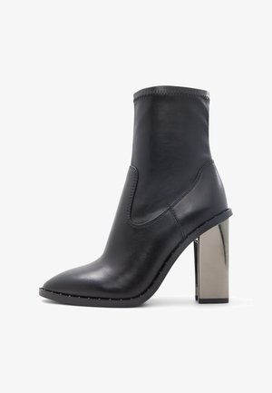 Stivale alla caviglia in pelle nera con punta affilata, lato elasticizzato e tacco a blocco metallico lucido. Presenta cuciture sottili lungo i bordi.
