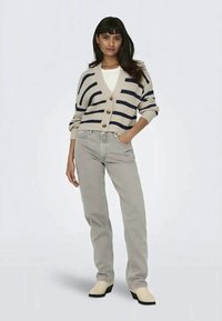 Beige striped cardigan with navy lines, button front, and cropped fit, paired with light gray jeans and cream slip-on shoes.
