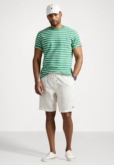 Tricou cu dungi verzi și albe, pantaloni scurți bej, adidași albi și o șapcă albă, având un mic logo albastru pe piept și pe pantaloni.