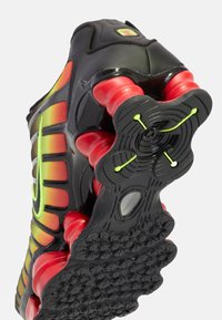 Nike-tennarit mustalla päällä, punaisella vaimennuksella, keltaisilla yksityiskohdilla ja teksturoidulla mustalla ultralle, jossa on pyöreitä kuvioita ja nypyköitä.