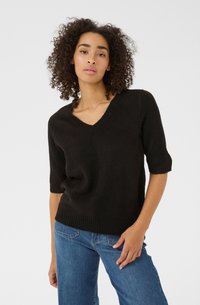 Svart kortärmad v-ringad tröja i mjukt, strukturerat tyg med ribbad nederkant. Buren tillsammans med blå denimjeans.