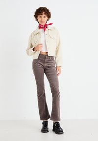 Cremefarvet fløjljakke, hvid crop top, grå fløjlsbukser, sorte chunky sko, rød bandana. Tekstilstruktur og lomme detaljer synlige.