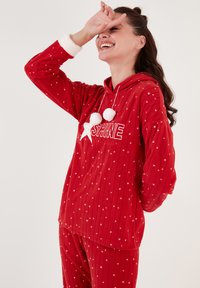 Röd luvtröjebyxa-set i plyschmaterial, med vitt stjärnmönster, ribbad textur och pom-pom detaljer vid halsringningen.