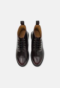 Burgundské kožené kotníkové boty s lesklým povrchem, černými tkaničkami a poutkem na patě. Mají zaoblenou špičku a textured podešev.