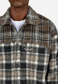 Πλαϊνός φλις μπουφάν σε καφέ, μαύρο και γκρι. Διαθέτει κουμπί κλεισίματος, γιακά και κεντημένο λογότυπο "Pegador" στο στήθος. Μαλακή υφή.