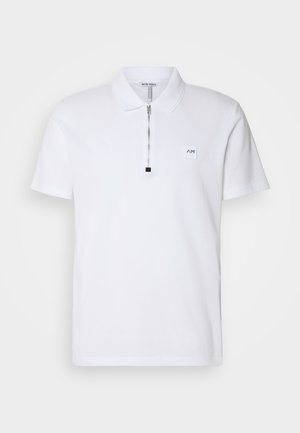 Valge polo särk, millel on lühike tõmblukk kaeluses, tikandiga logo rinnal ning pehme puuvillane materjal sujuva tekstuuriga.