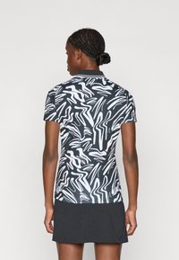Camisa polo de manga curta em preto e branco com um padrão abstrato de ondas, com colarinho preto e uma silhueta ligeiramente ajustada.