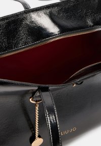 Borsa tote in pelle verniciata nera con hardware dorato, caratterizzata da un'esterno lucido, un rivestimento interno rosso e un accent decorativo a catena.