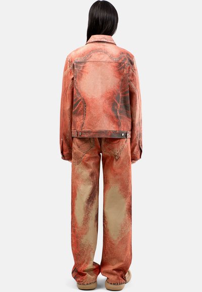 Chaqueta y pantalones de mezclilla en tonos naranjas y beige con una textura desgastada. Presenta costuras visibles y un ajuste relajado.