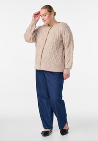 Beigais adīts kardigans ar dimantu rakstu, ar noapaļotu kaklu un pogām. Saskaņots ar zilām džinsu biksēm un melnām čībām.