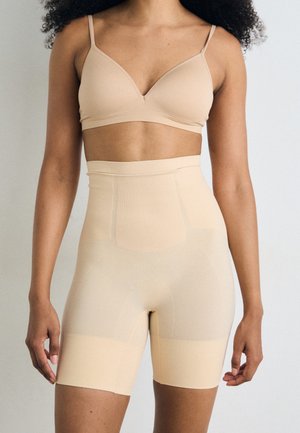Soutien-gorge beige sans coutures et shorts taille haute, tous deux dotés d'une texture lisse et extensible ainsi que de panneaux de modelage discrets, conçus pour le confort.