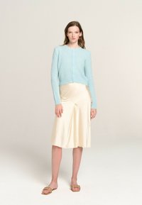 Light blue, fuzzy knit cardigan with round neck and button closure, paired with a cream satin slip skirt, and beige woven slip-on sandals.