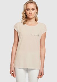 Kortermet beige t-skjorte laget av mykt stoff, med rund hals og en subtil "elsk deg selv" grafikk foran.