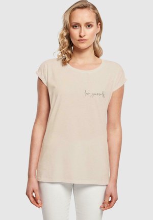 Kortermet beige t-skjorte laget av mykt stoff, med rund hals og en subtil "elsk deg selv" grafikk foran.