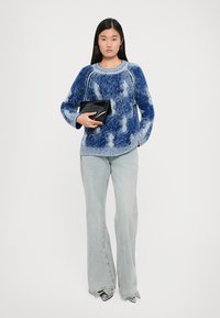 Pulover albastru cu un model texturat, guler rotund și manșete evazate, combinat cu blugi evazați de culoare albastru deschis și o geantă clutches neagră.
