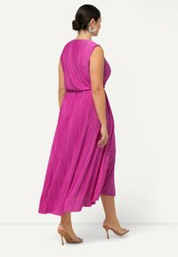 Růžové plisované maxi šaty bez rukávů, se stáhnutým pasem a splývavou sukní. K tomu nazouvací sandály na vysokém podpatku v tělové barvě. Hladká textura.