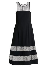 Robe noire sans manches longueur genou avec des panneaux en mesh à pois transparents au niveau de l'encolure et de l'ourlet, et une petite fermeture par bouton à l'arrière.