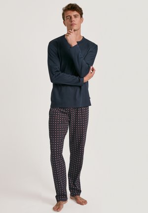 Marineblauwe longsleeve top gecombineerd met tapse pyjamabroek met een herhalend bloemmotief in rood en wit op een donkere achtergrond.
