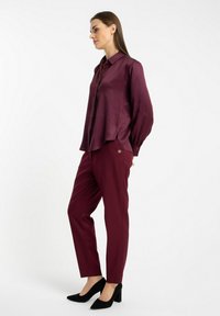 Burgundowa jedwabna bluzka z kołnierzykiem i długimi rękawami, zestawiona z dopasowanymi spodniami ołówkowymi z małym złotym akcentem. Czarne szpilki.