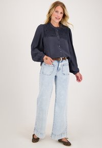 Marineblouse met kantdetails op de schouders, knoopsluiting en pofmouwen, gecombineerd met lichtblauwe wijde jeans en leopardenprint slippers.