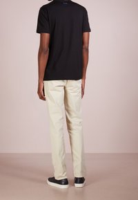 T-shirt en coton noir, pantalon crème et baskets noires. Le t-shirt présente un petit logo bleu au dos. Texture lisse, coupe décontractée.