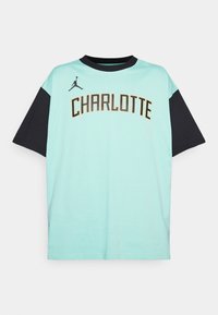 Camiseta de manga corta en azul claro con detalles en negro, que presenta "CHARLOTTE" en letras doradas en negrita y un pequeño logotipo de Jordan en negro.