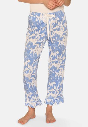 Woman wearing blue and white floral print pajamas with ruffled cuffs and a white drawstring waist, standing barefoot.