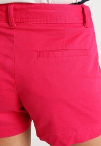 Růžové bavlněné šortky s hladkou strukturou a viditelnou zadní kapsou. Mají upravený pas a krátkou délku nohavic.