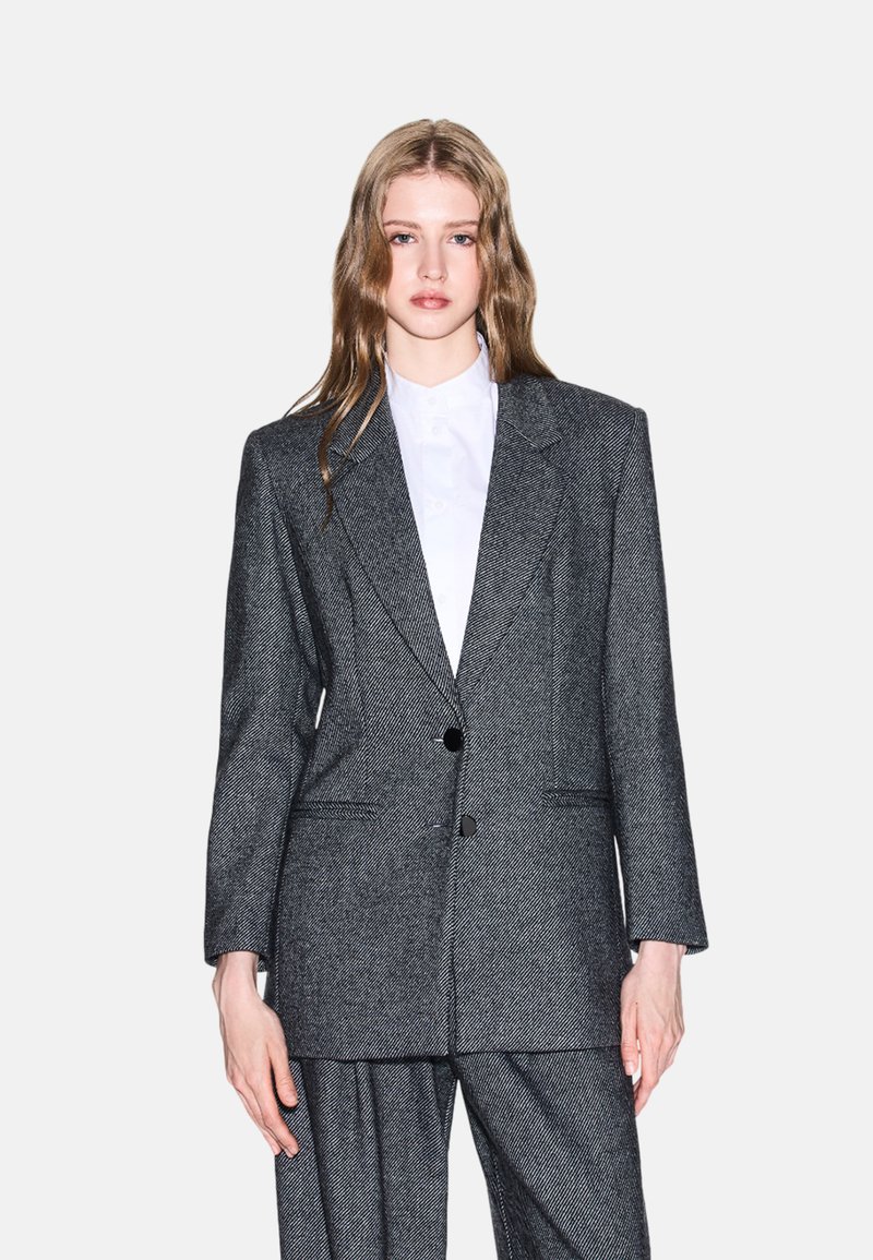 Blazer grigio a spina di pesce in tessuto testurizzato, monopetto con due bottoni, rever a scialle e tasche laterali. Adatto a look sartoriali.