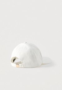 Λευκό καπέλο μπέιζμπολ με καμπύλη γείσο, ρυθμιζόμενο λουράκι στο πίσω μέρος και υφασμάτινη υφή. Διαθέτει μικρό μεταλλικό διακοσμητικό στο λουράκι.