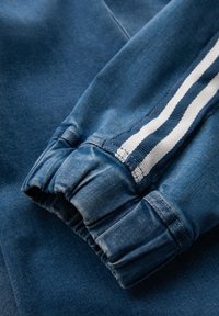 Blå denimtyg med en rynkad mudd. Har en sidrand i vitt och marinblått. Mjuk textur med lätt blekning nära sömmen.